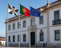 Bandeira de Portugal entre uma bandeira municipal e a bandeira da União Europeia junto a um edifício público