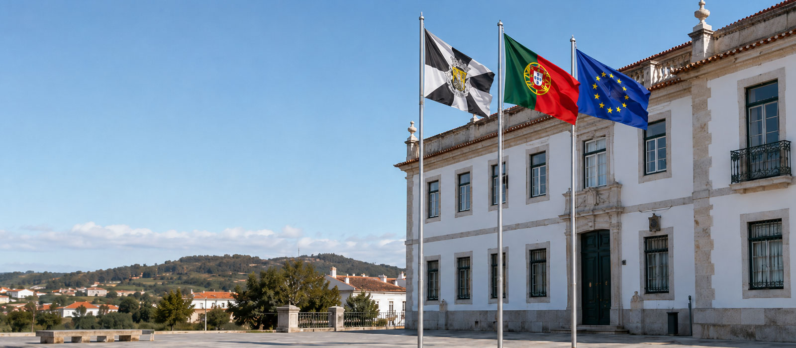 Bandeira de Portugal entre uma bandeira municipal e a bandeira da União Europeia junto a um edifício público